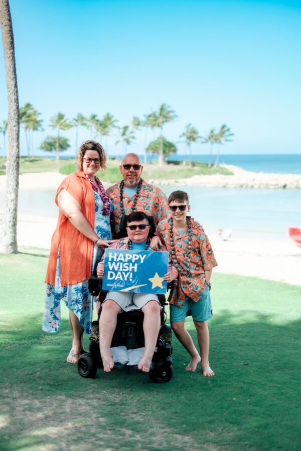 Ethan with his family on a beach holding a "happy wish day" sign